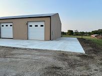Tan metal building with white garage doors and concrete pad.