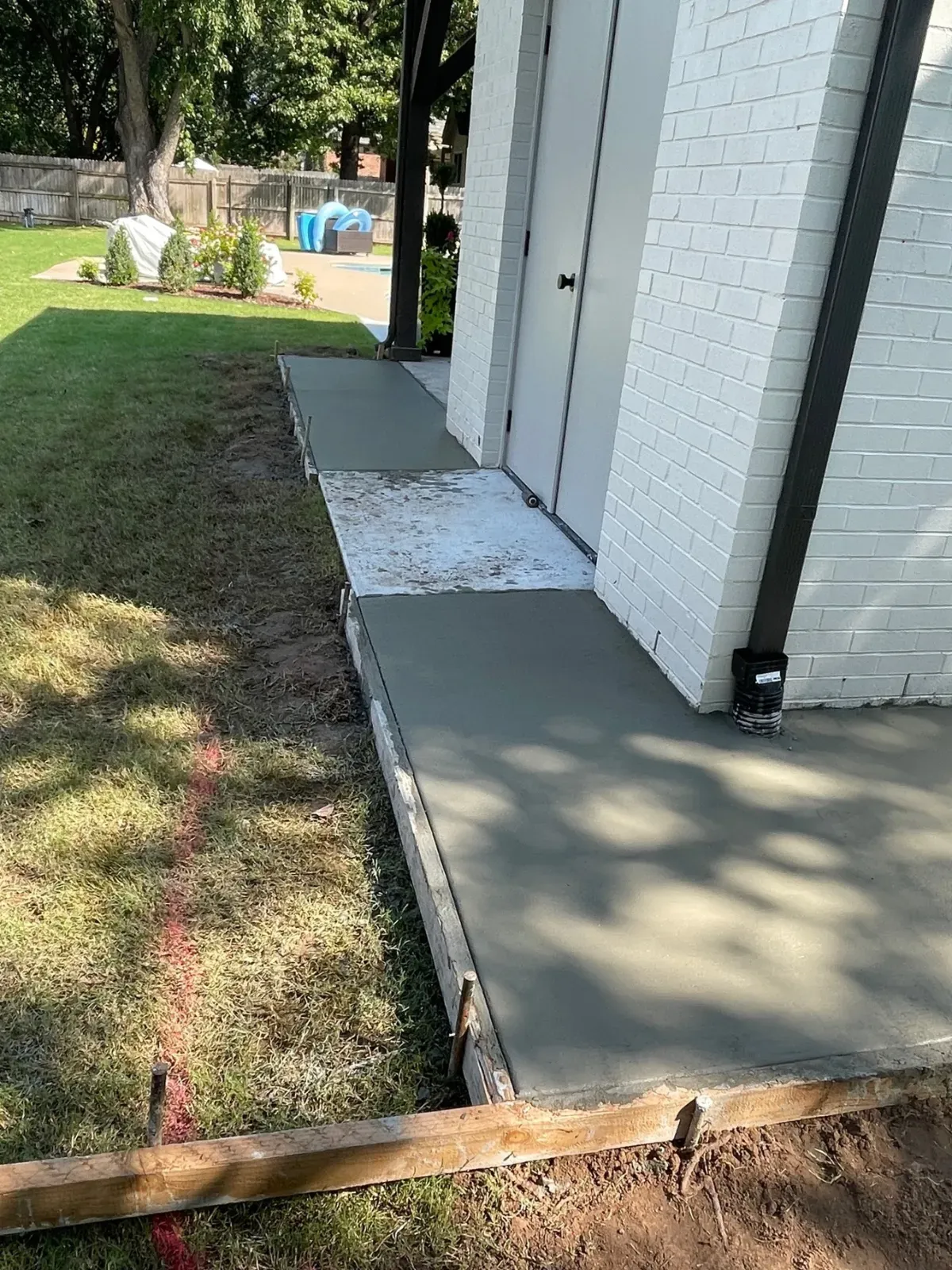 Concrete walkway alongside a white brick building, next to a grassy lawn, with a red string line.