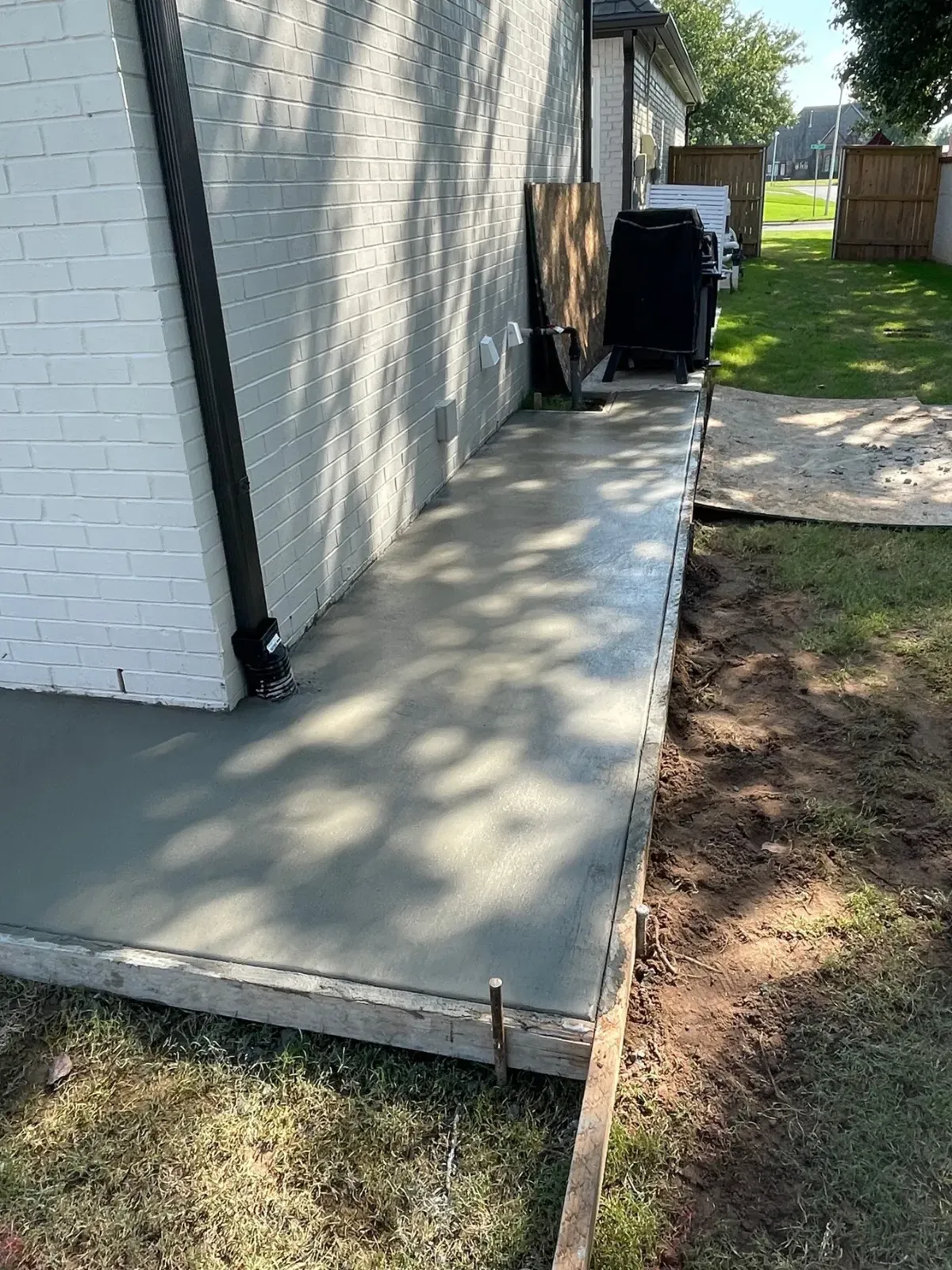 Newly poured concrete walkway next to a white brick building, with a black downspout.
