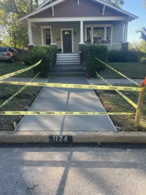 Freshly poured concrete sidewalk with caution tape in front of a house, with the number 1124 visible.