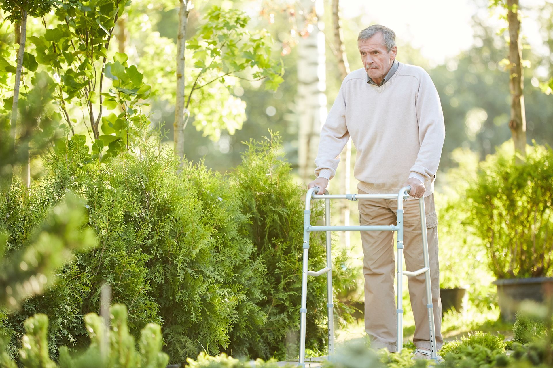 Ein älterer Mann benutzt einen Rollator in einem Park.