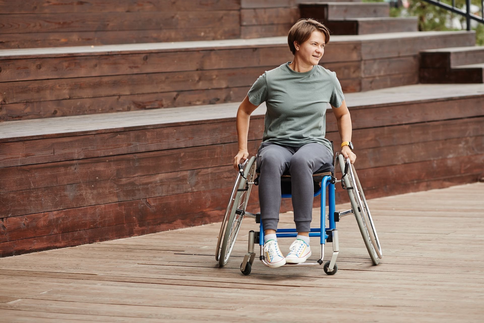 Eine Frau sitzt in einem Rollstuhl auf einem Holzdeck. Querschnittslähmung Ergotherapie