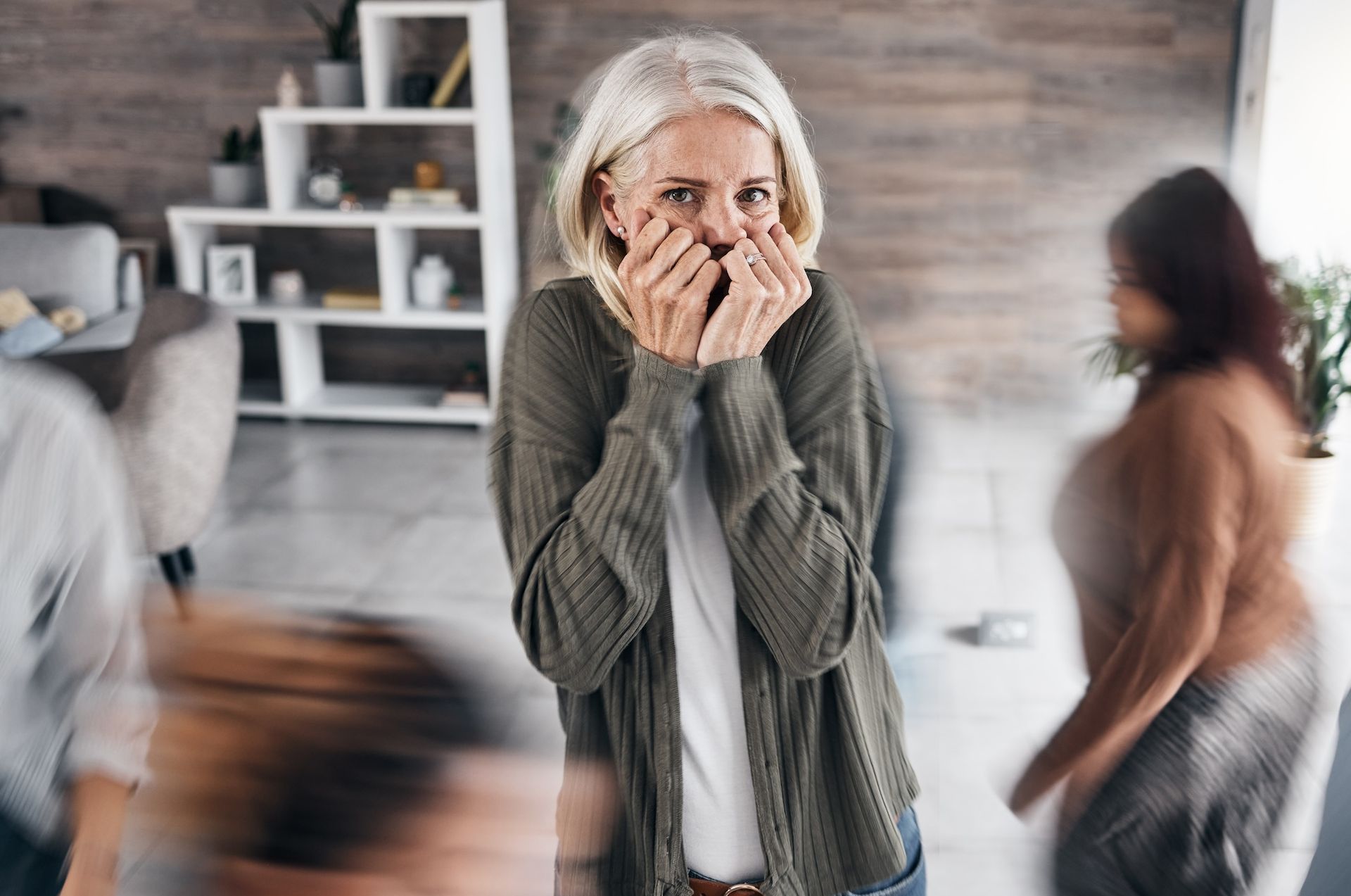 Eine Frau bedeckt ihren Mund mit den Händen, während sie vor einer Menschenmenge steht und Angst hat. Schizophrenie mit Ergotherapie