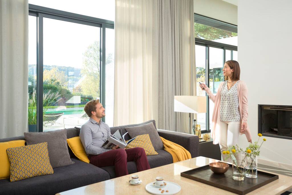 A woman is standing next to a man sitting on a couch in a living room.