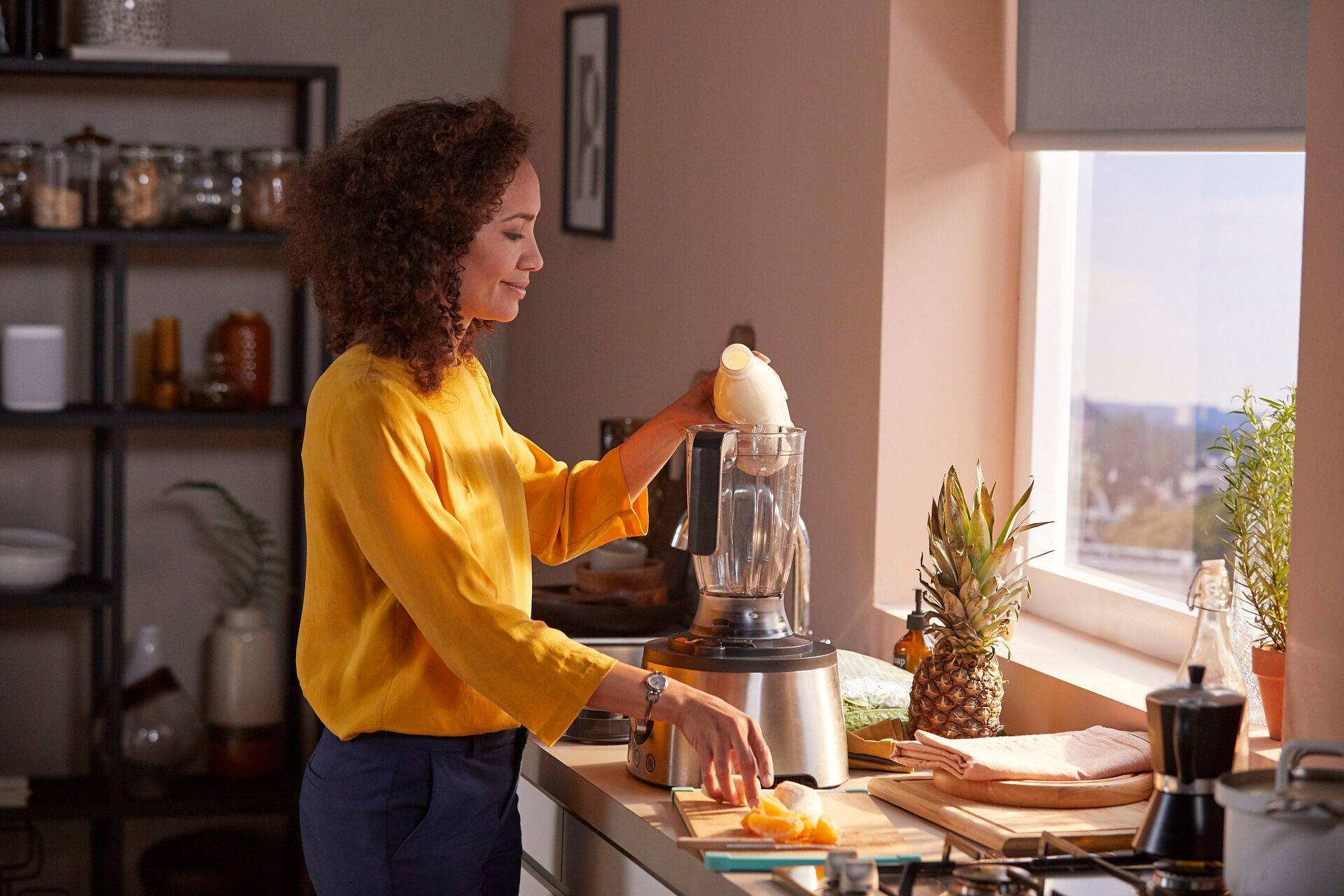 A woman is making a smoothie in a blender in a kitchen.