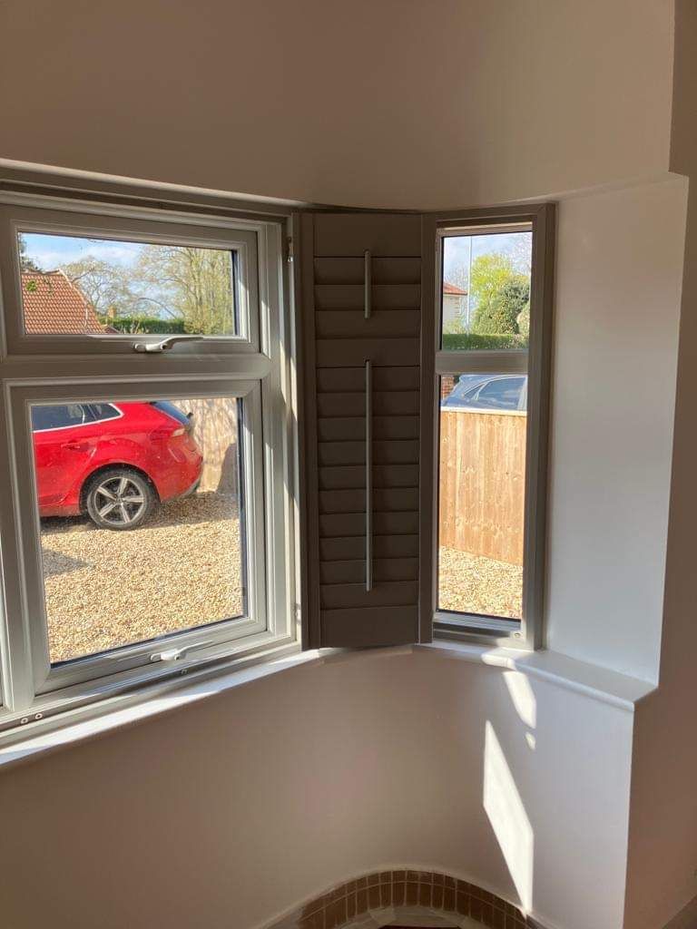 A red car is parked in front of a window with shutters.