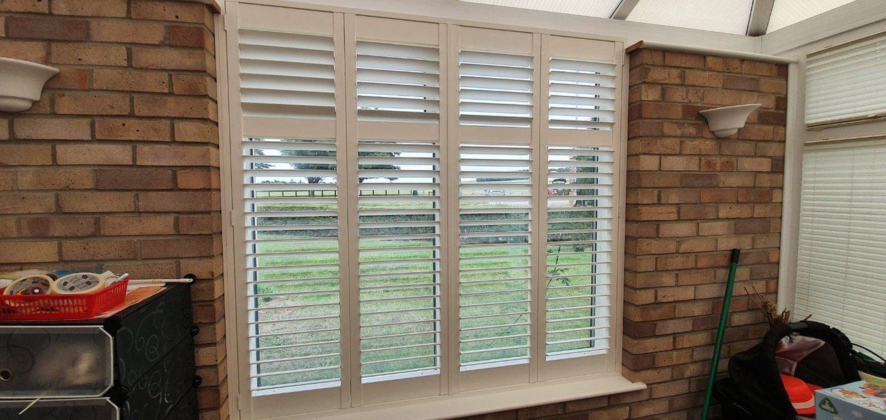 A window with shutters on it is in a room with a brick wall.