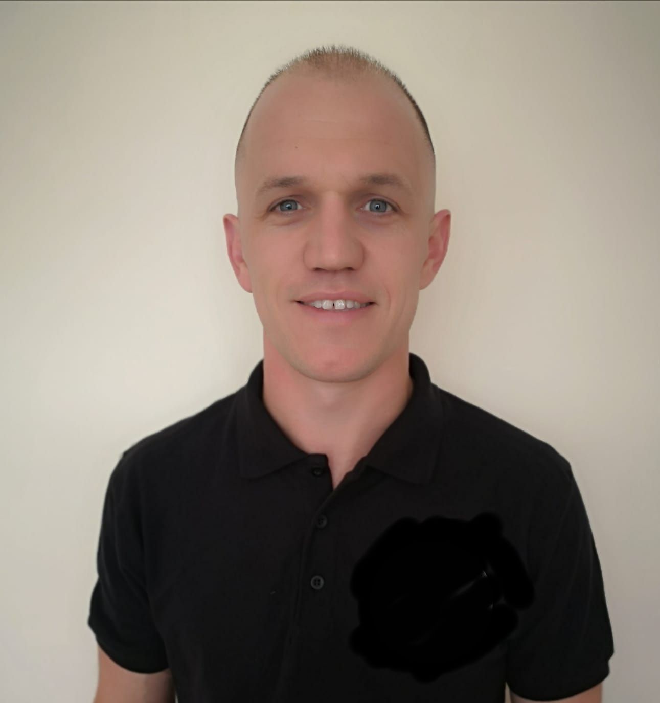 A man wearing a black polo shirt is smiling for the camera