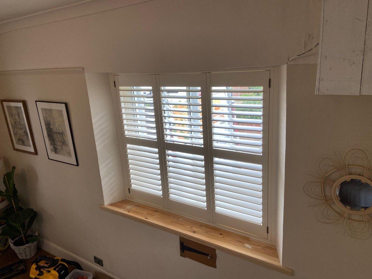 A living room with a window with white shutters on it.
