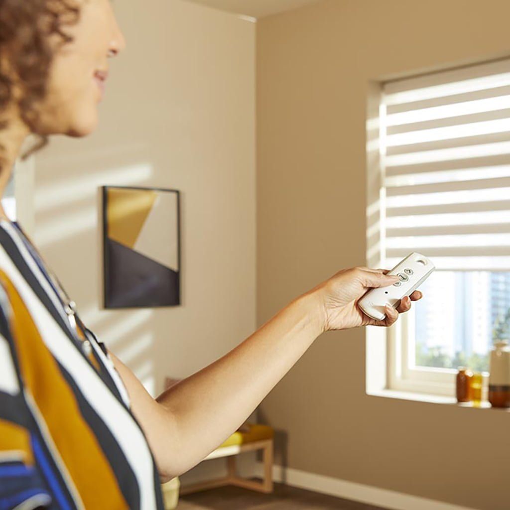 A woman is holding a remote control in front of a window.