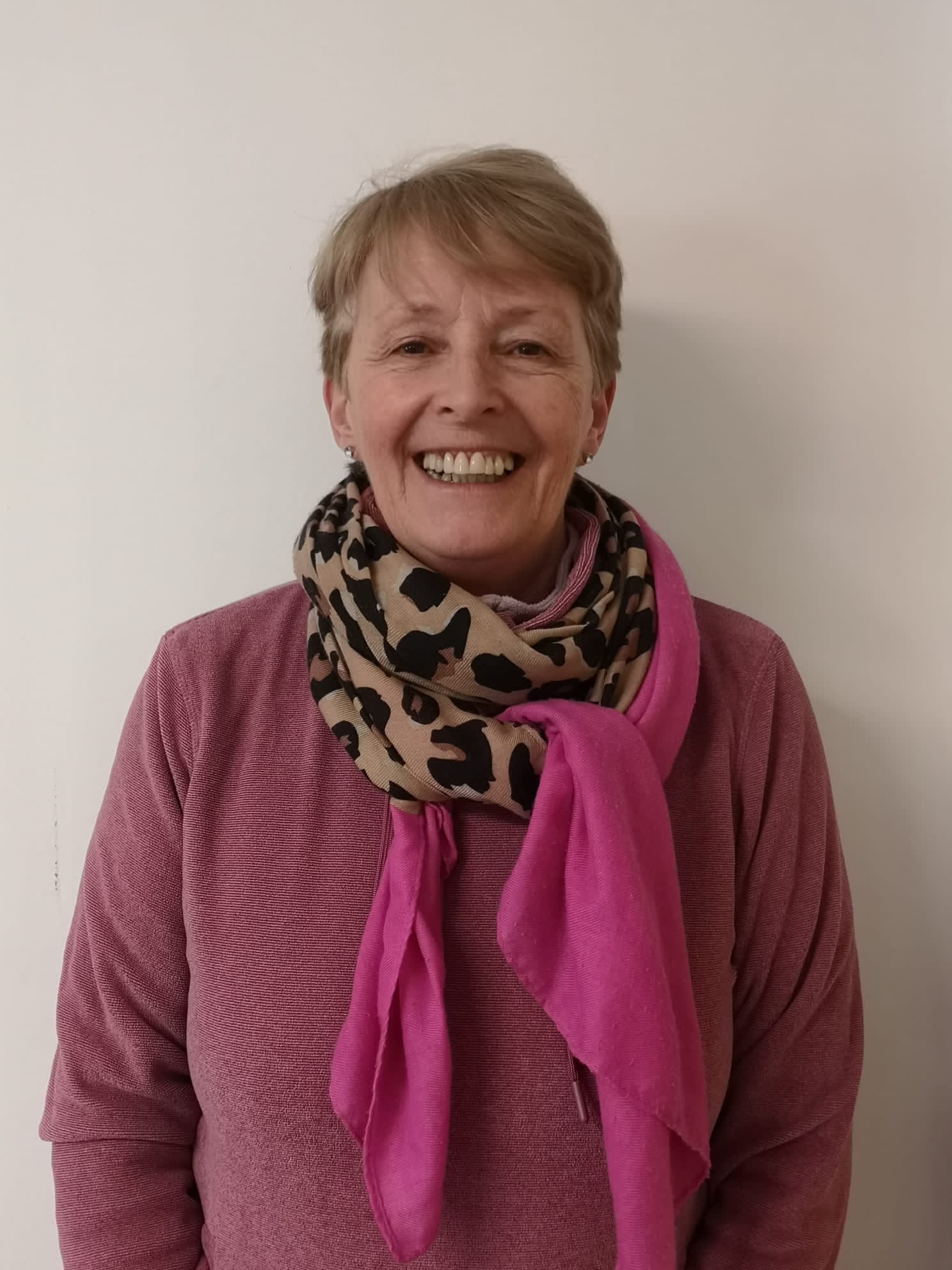 A woman wearing a pink sweater and a pink scarf is smiling.