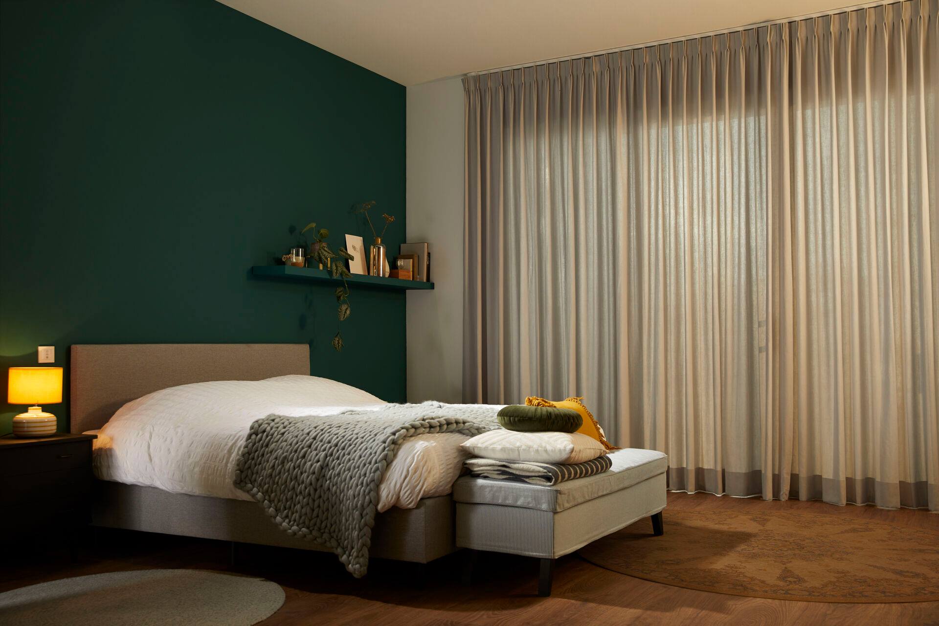 A bedroom with a bed , nightstand , lamp and curtains.