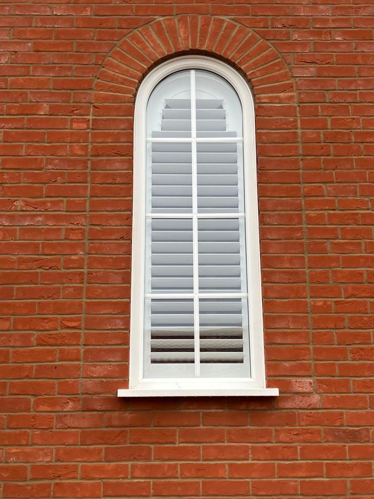 A white window with shutters on a red brick wall.