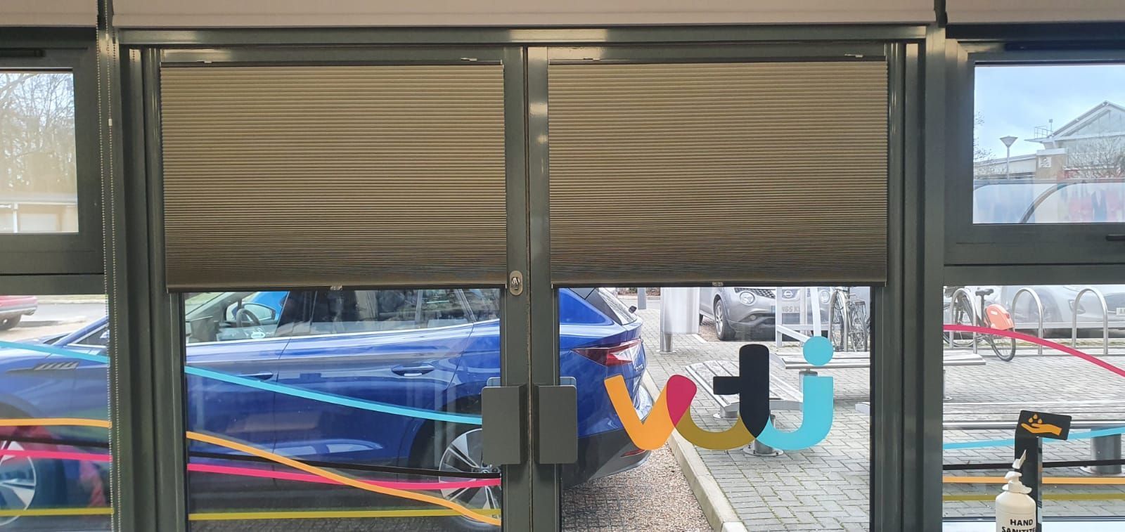 A blue car is parked in front of a glass door.