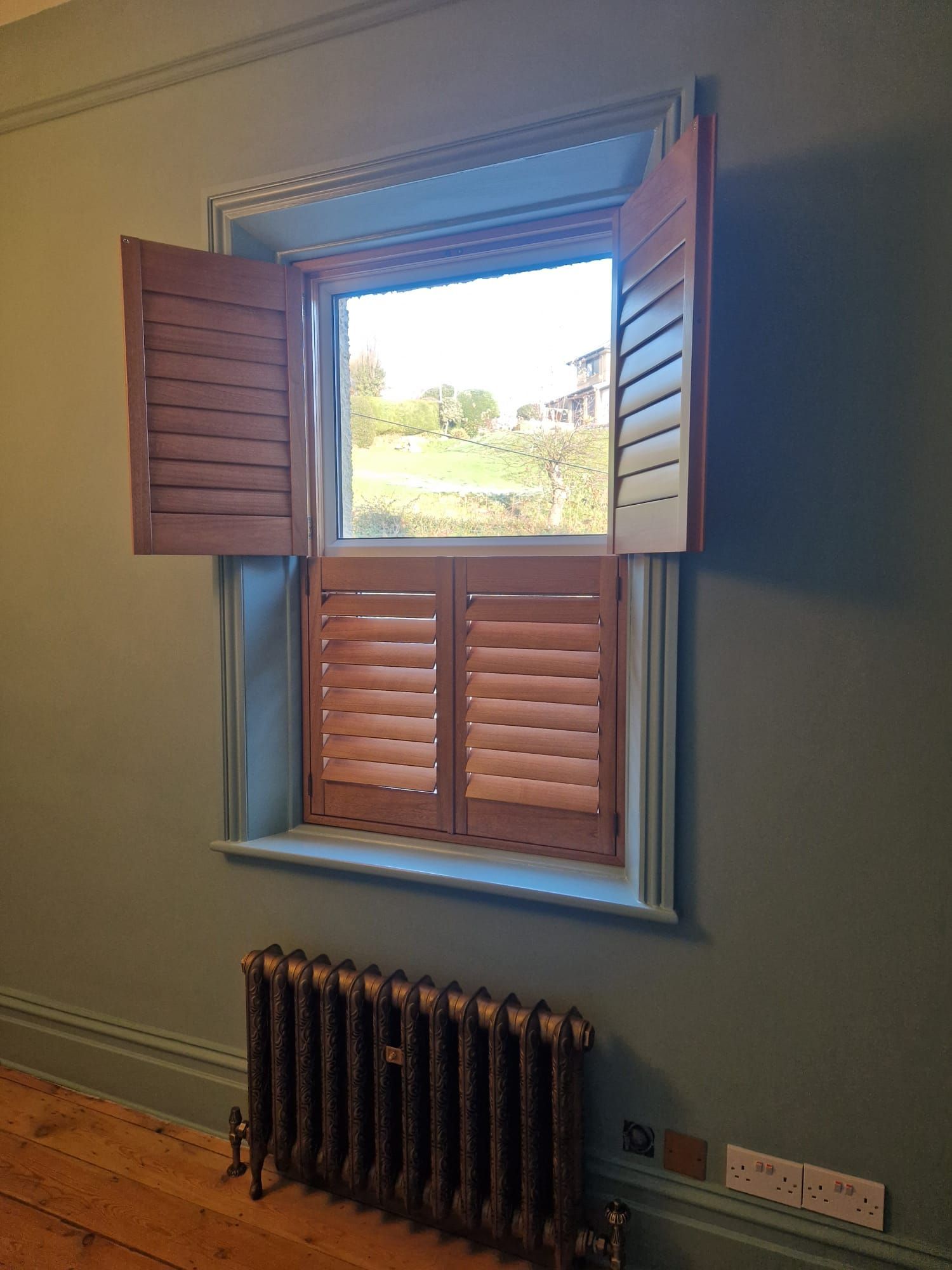 A window with wooden shutters and a radiator in a room.
