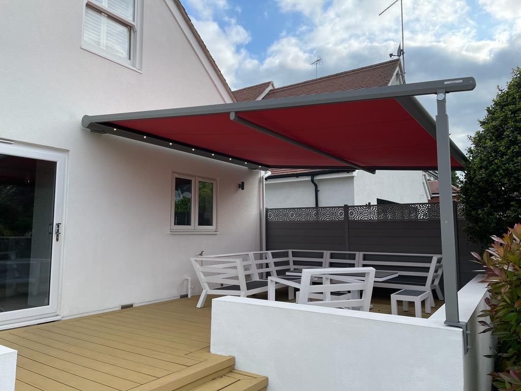 A white house with a red awning over a patio with tables and chairs.