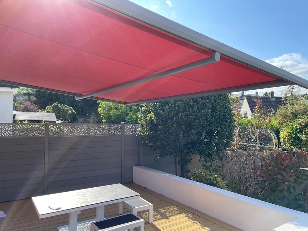 A red awning is covering a patio with a table and chairs.