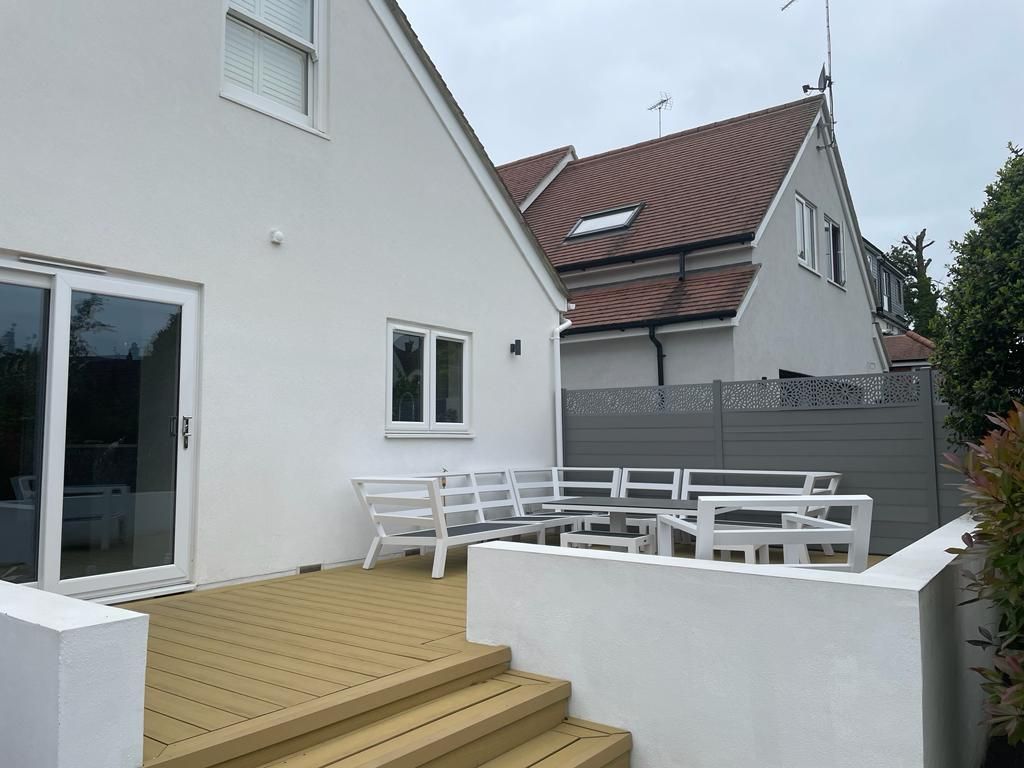 A white house with a wooden deck and stairs in front of it.