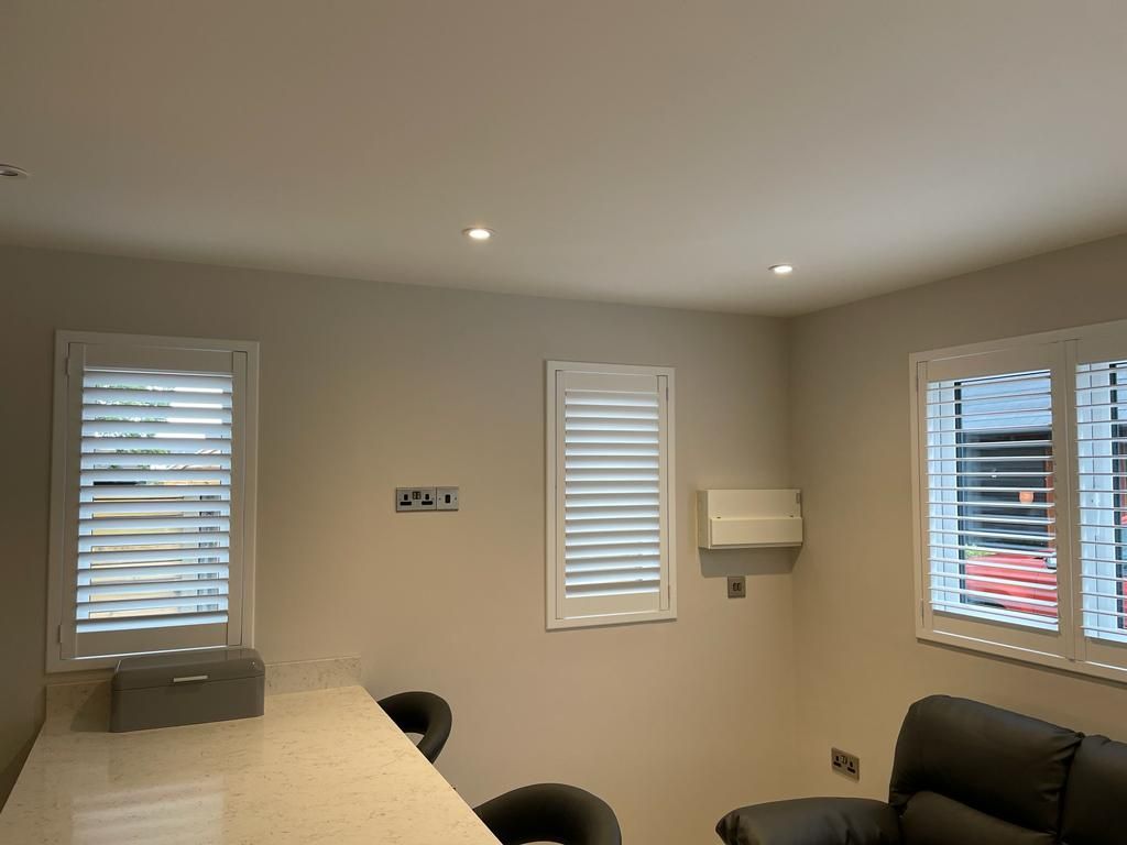 A living room with a couch , table , chairs and shutters on the windows.