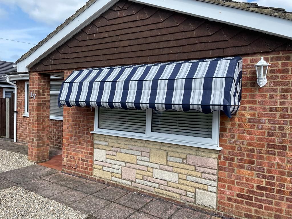 A brick house with a blue and white striped awning over a window.