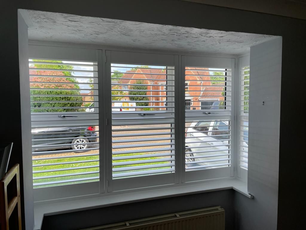 A window with shutters on it and a car parked in the background.