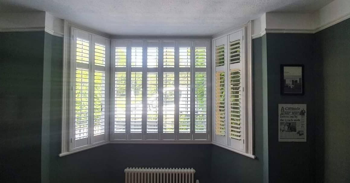 A room with a large bay window with shutters on it.