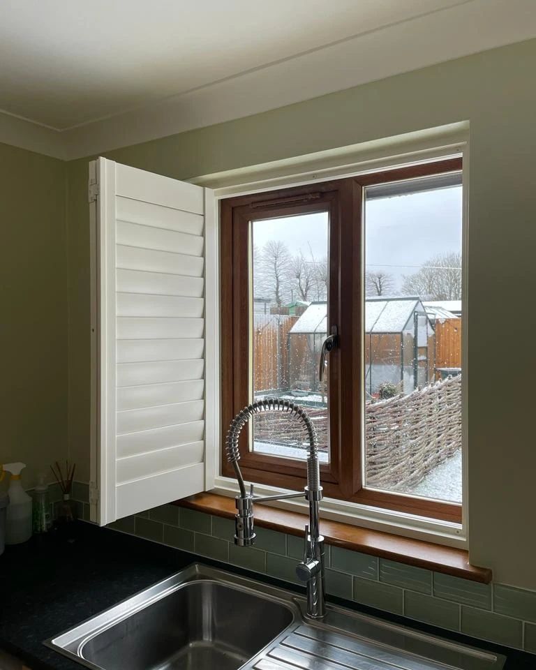 A kitchen with a sink and a window with shutters on it.