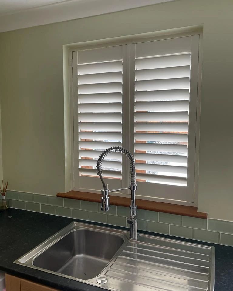 A kitchen sink with a faucet and shutters on the window.