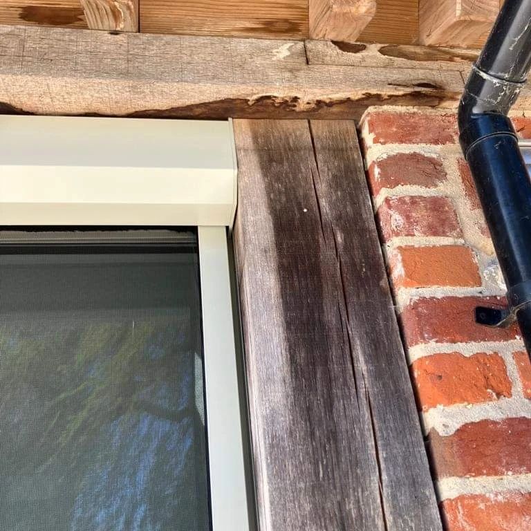 A window with a screen on it is sitting next to a brick wall.