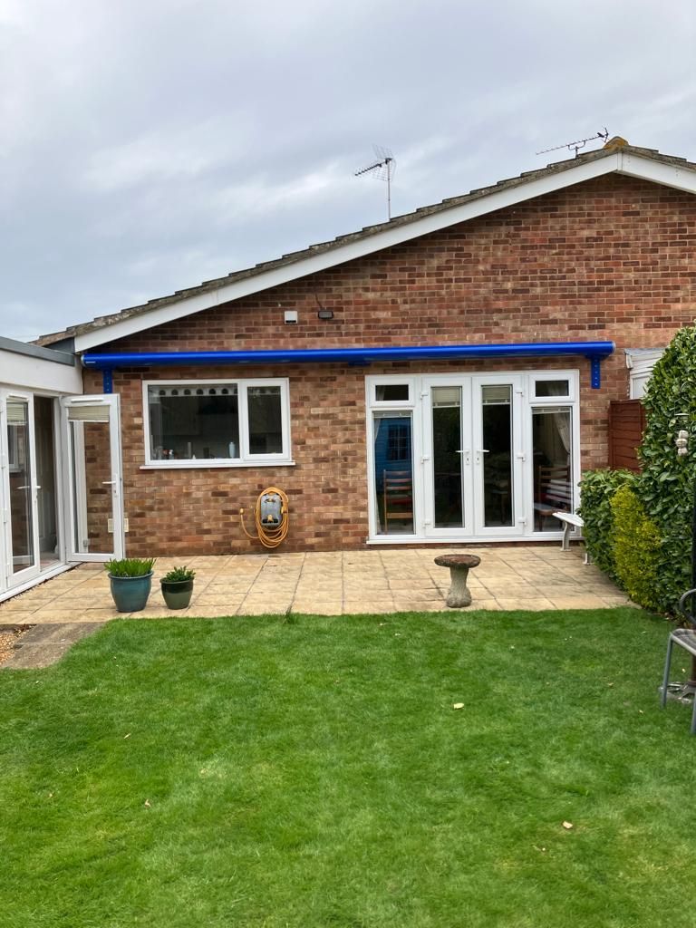 A brick house with a blue awning on the roof and a large lawn in front of it.
