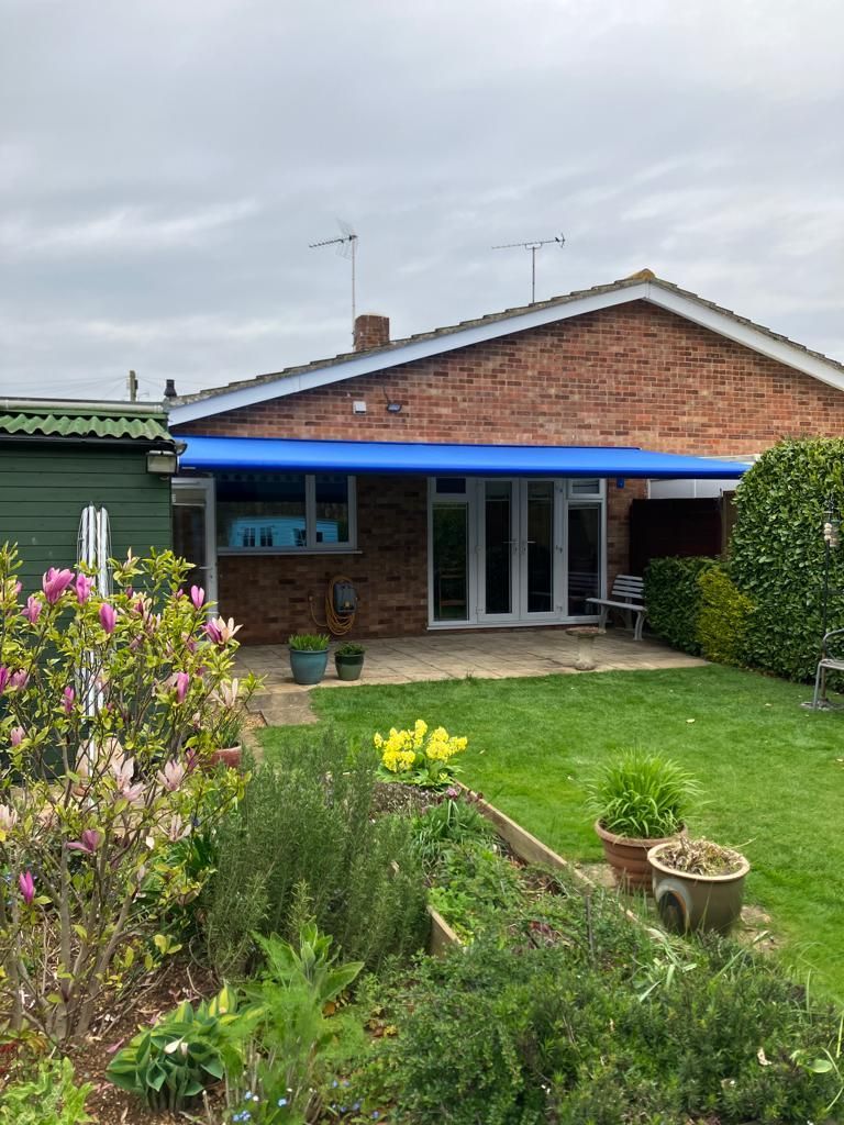 A brick house with a blue awning over the backyard.