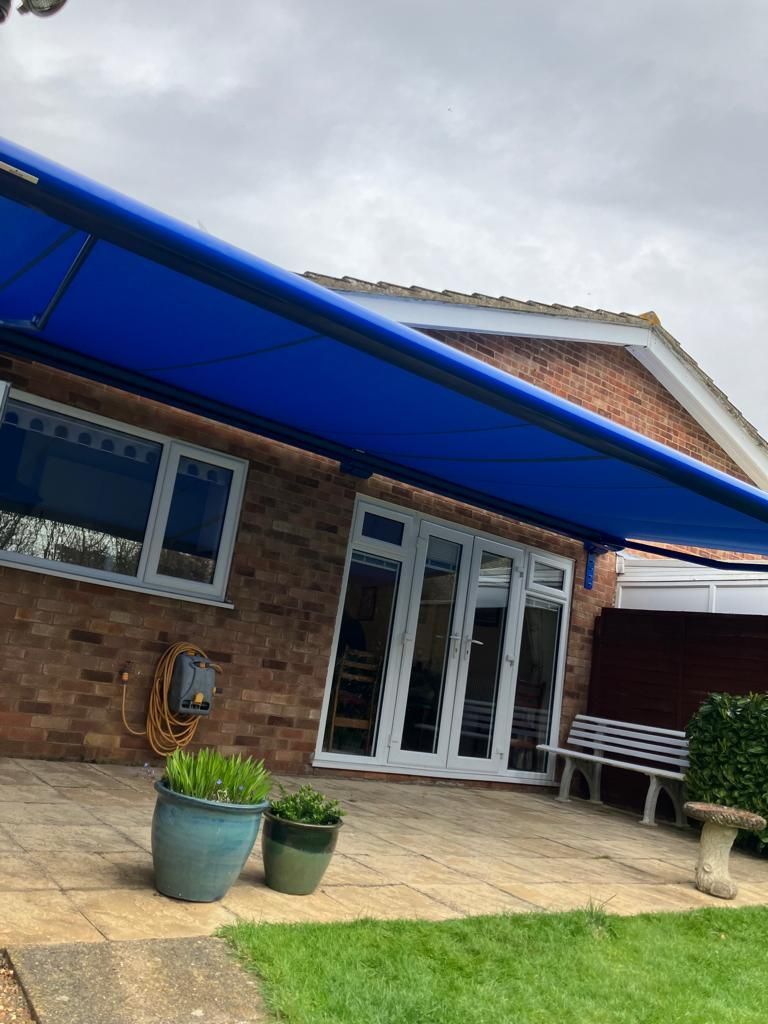 A blue awning is covering a patio in front of a brick house.
