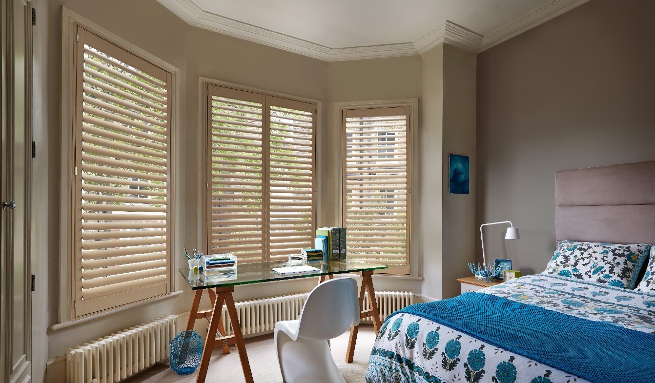 A bedroom with a bed , desk , chair and shutters on the windows.