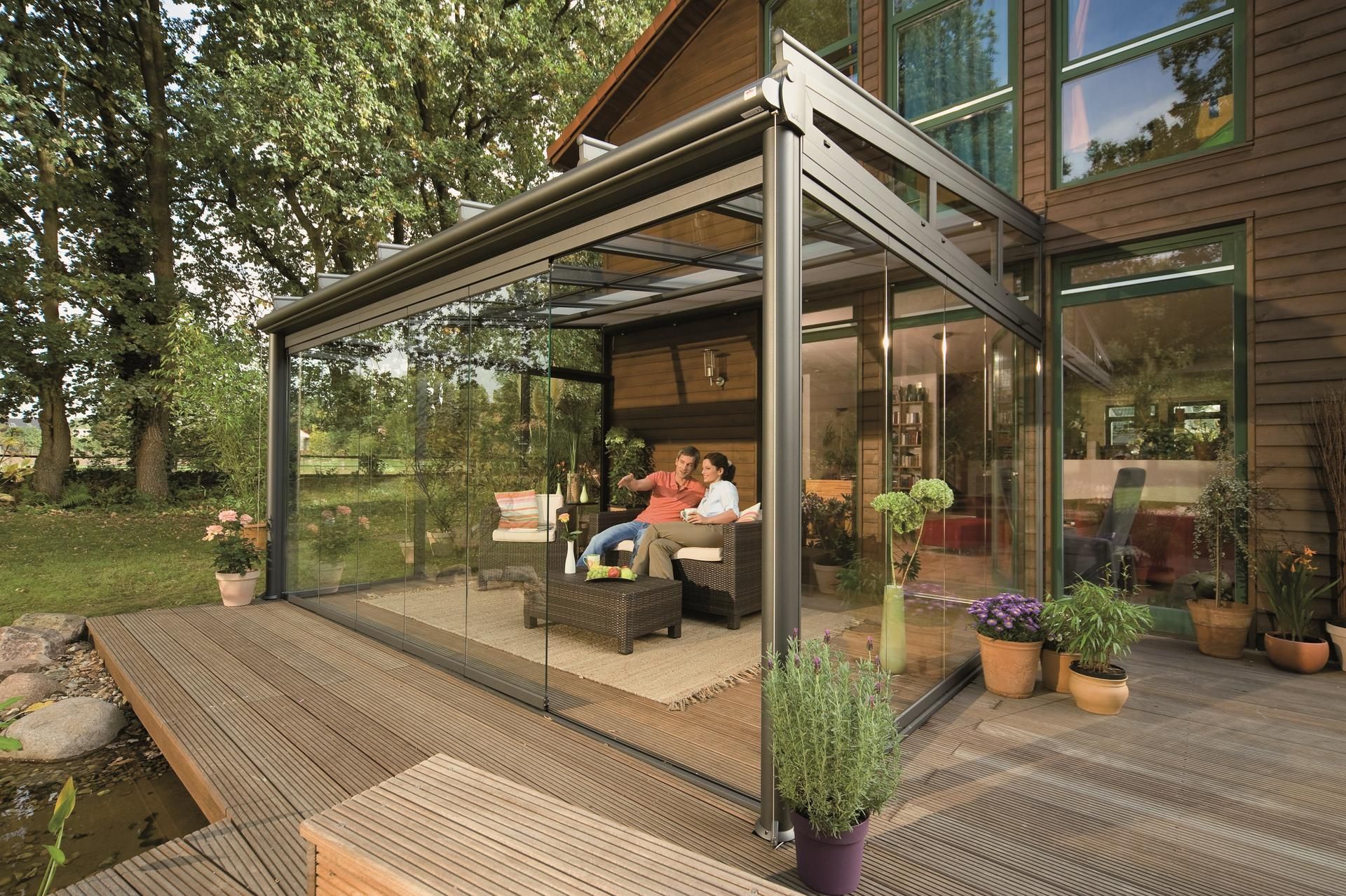 A couple is sitting on a couch under a glass covered patio.
