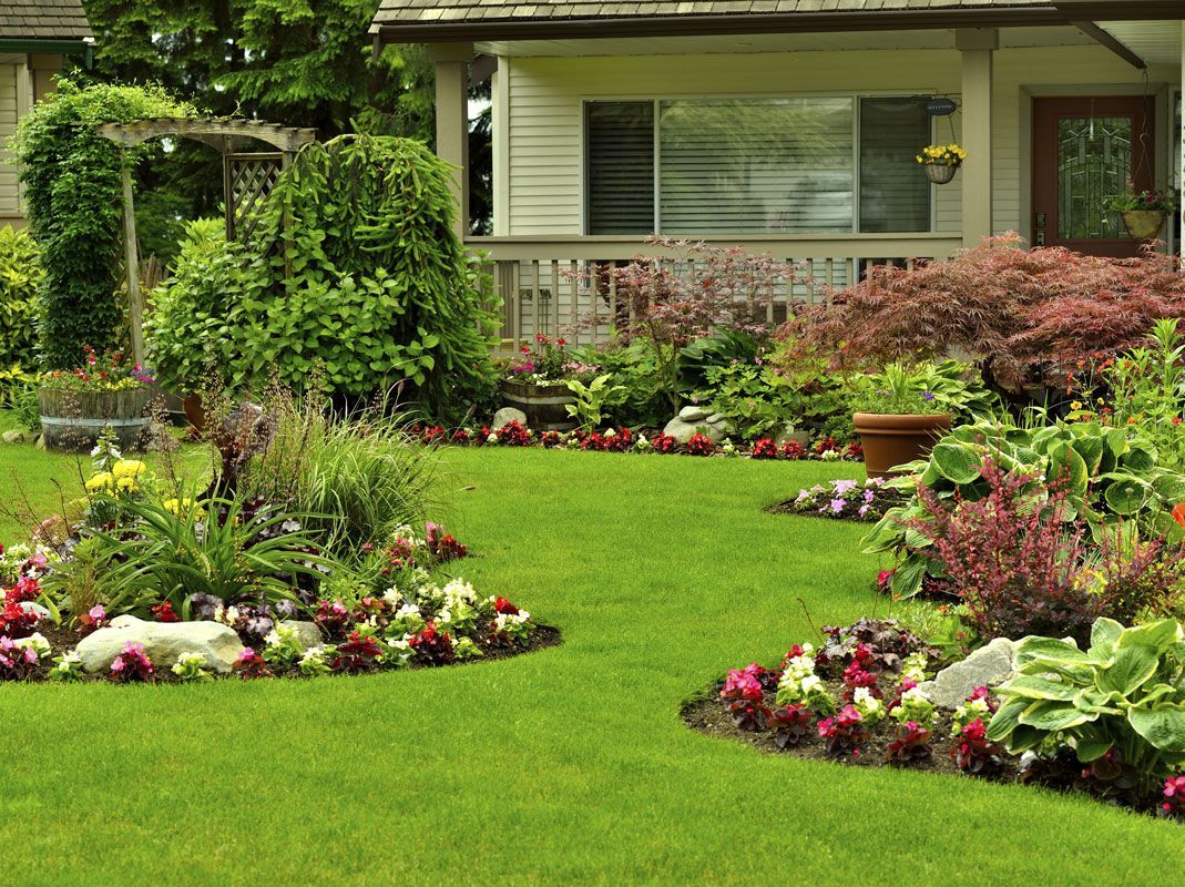Well-manicured front yard with green grass, flower beds, and a house in the background.