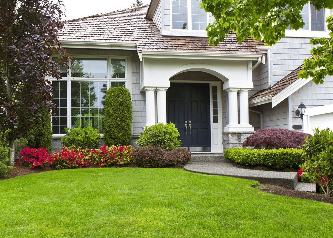 Gray house with blue door and lush green lawn and garden.
