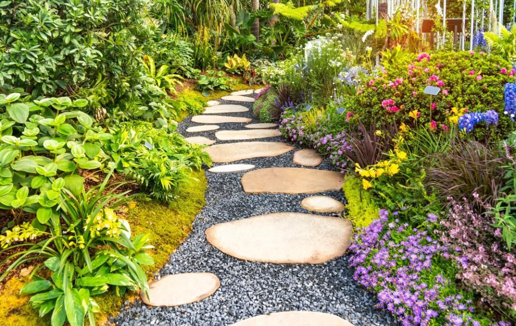 Stone pathway winds through lush garden with colorful flowers.