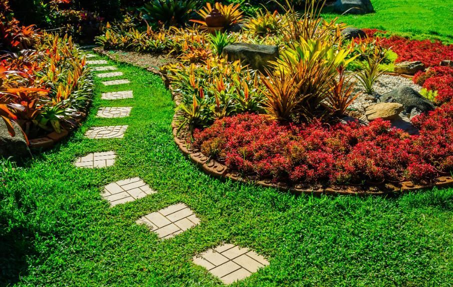 Stone path winds through vibrant garden beds with colorful foliage.