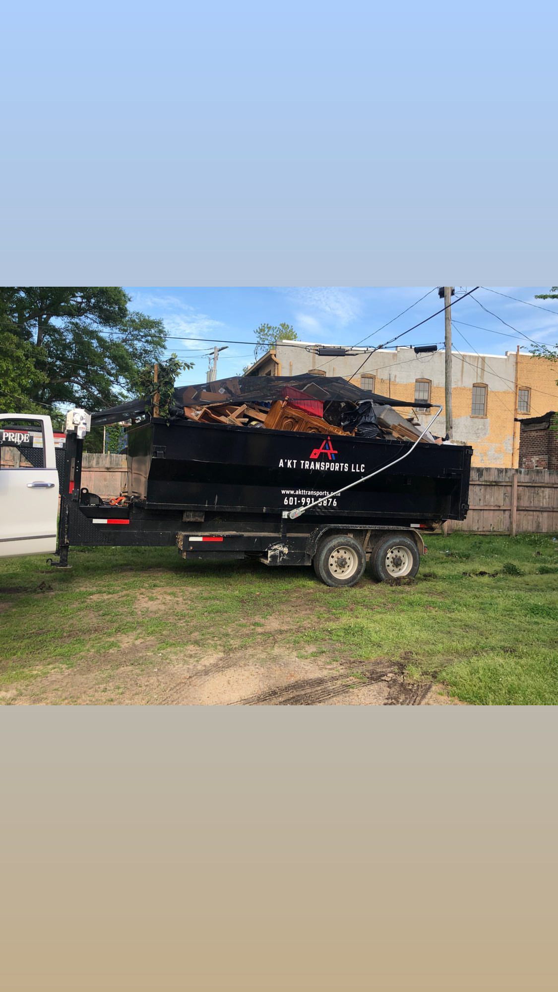A dumpster is being towed by a truck in a grassy area.