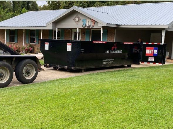 A dumpster is parked in front of a house on a trailer.