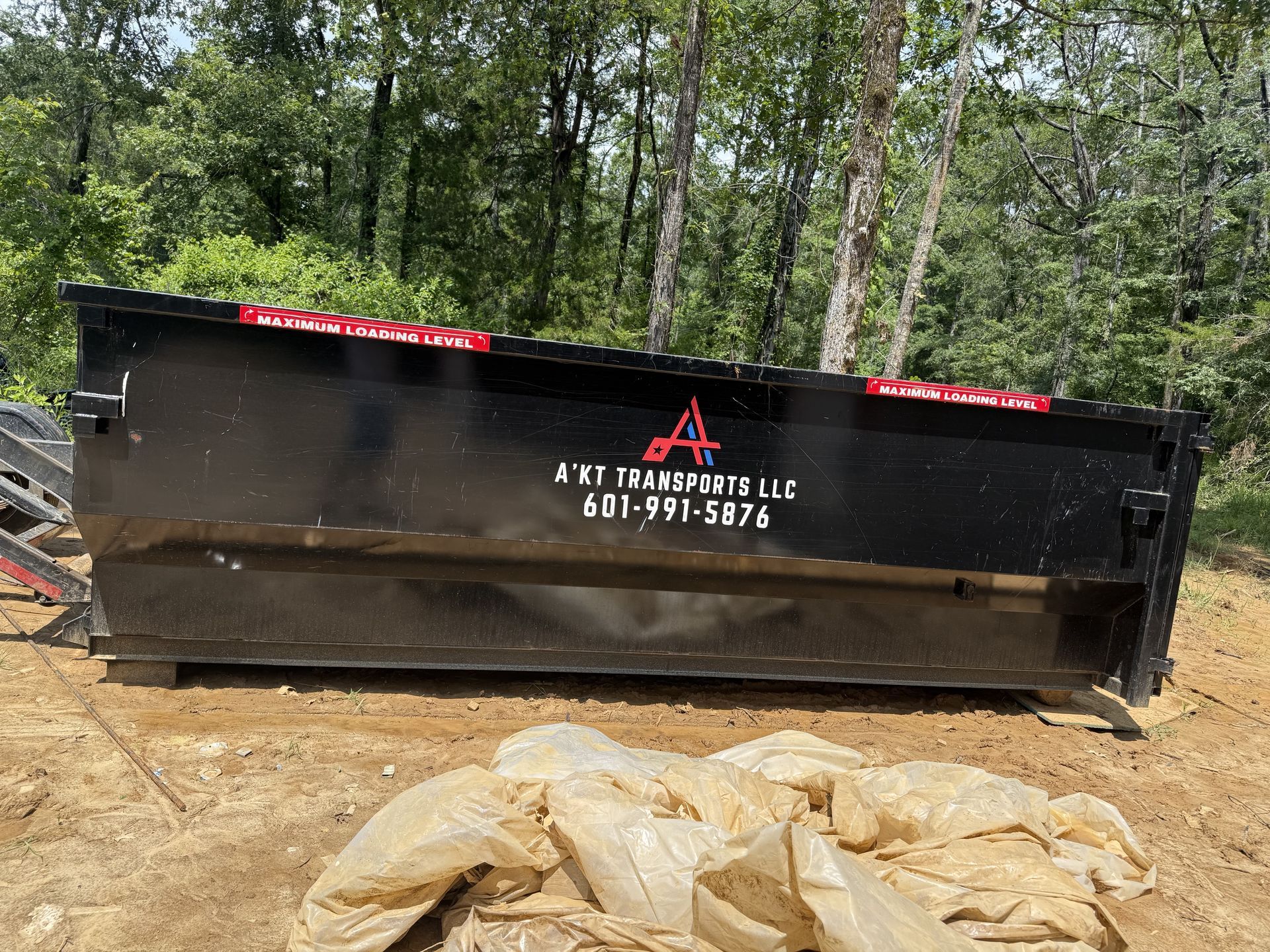 A large black dumpster is sitting on top of a dirt field.
