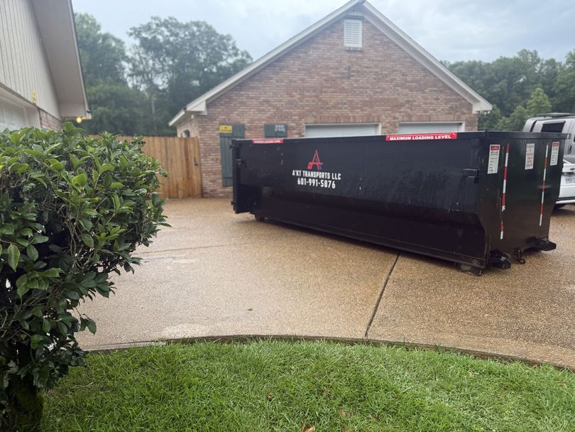 A large black dumpster is parked in front of a brick house.