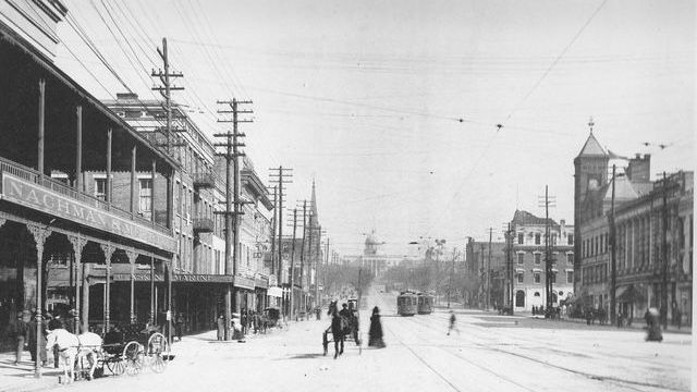 A black and white photo of a city street with horse drawn carriages