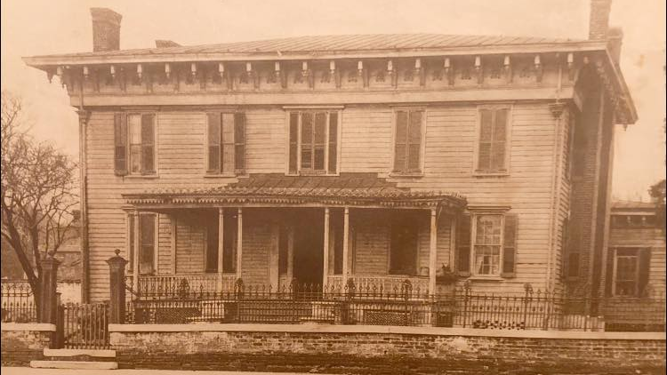A black and white photo of a large house with a porch.
