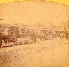 A black and white photo of horse drawn trolleys on a city street.