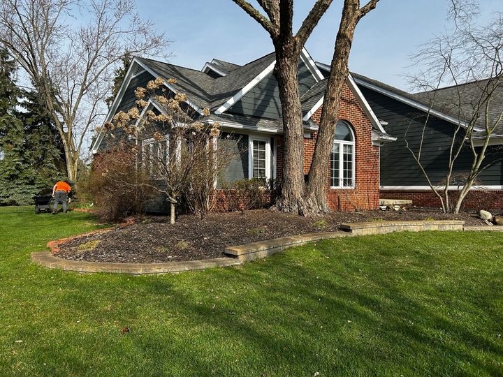 House with blue siding, red brick, and a tree in front. A lawn mower is visible on the left.