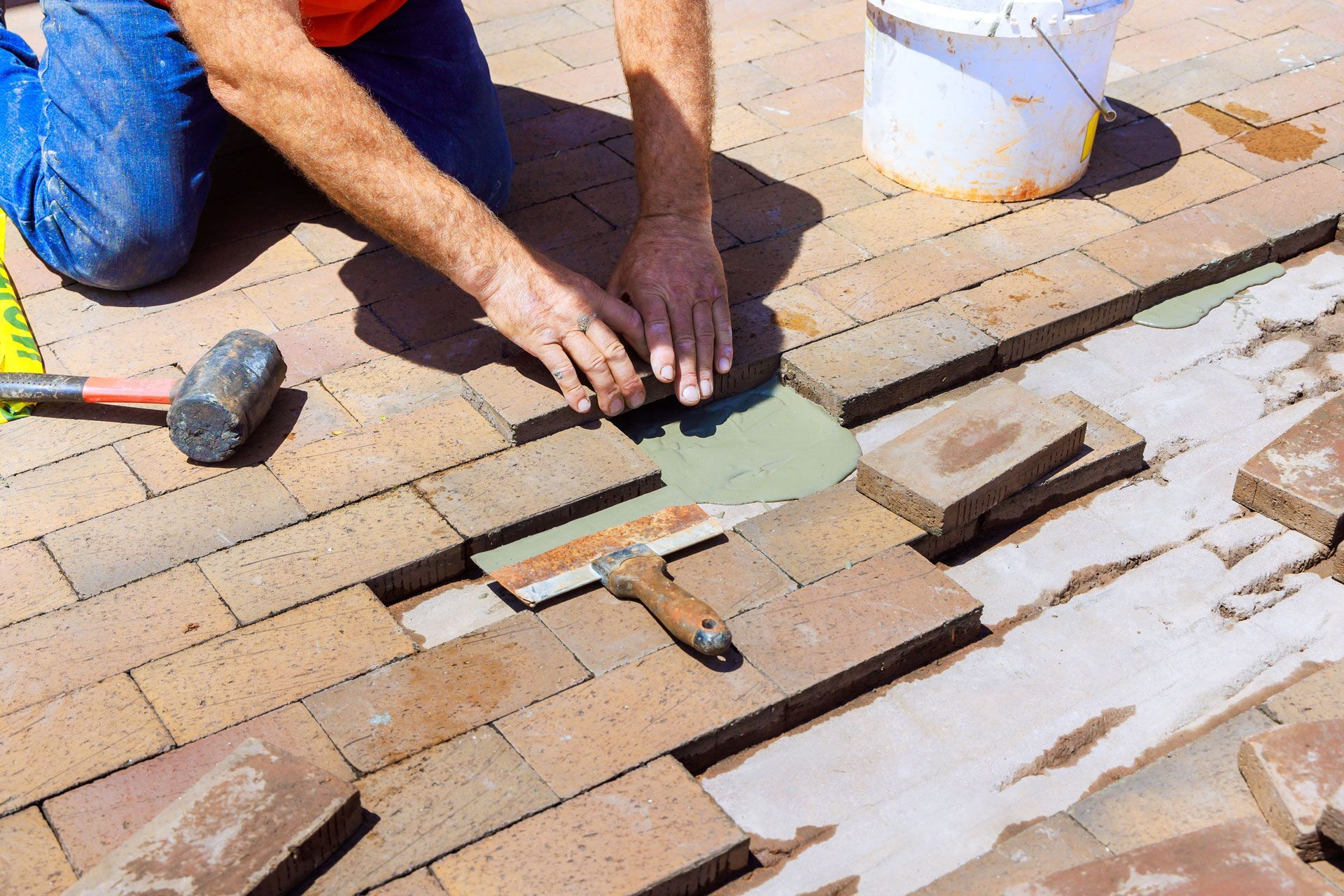 Worker laying paving tiles with a trowel and mallet on a patio
