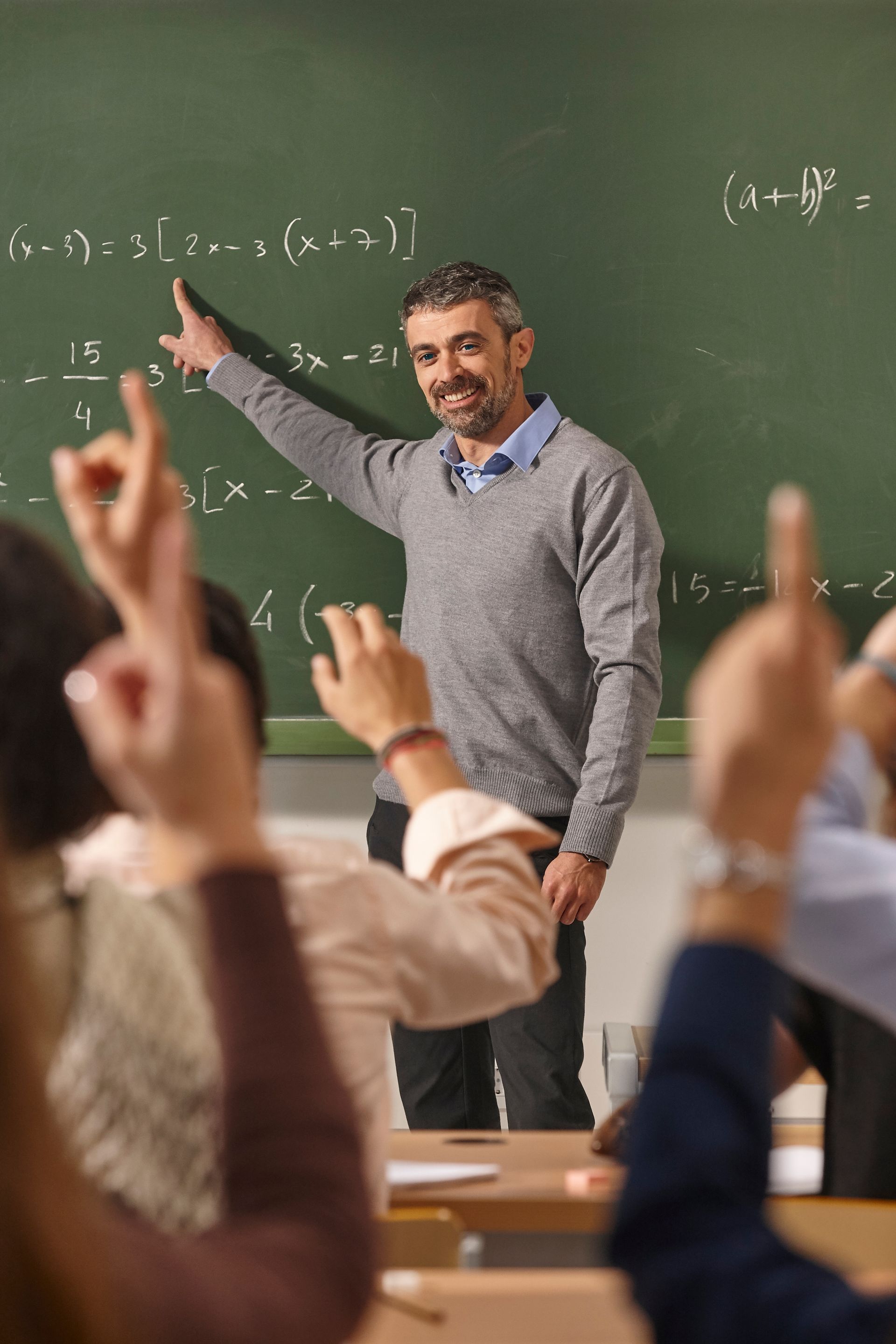 A man is standing in front of a blackboard teaching a class of students.