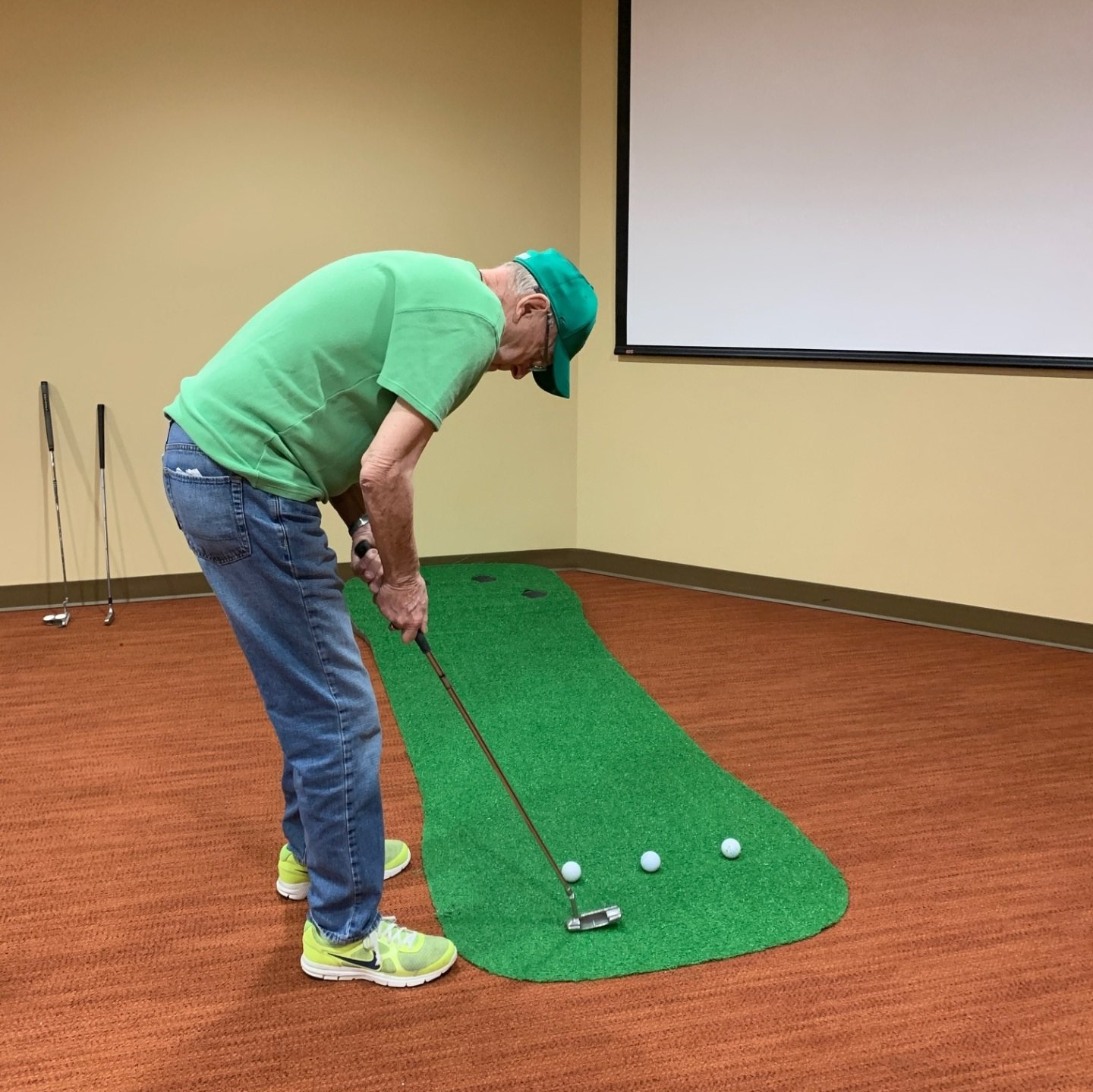 man playing mini golf indoors on a stripe of turf in senior living community
