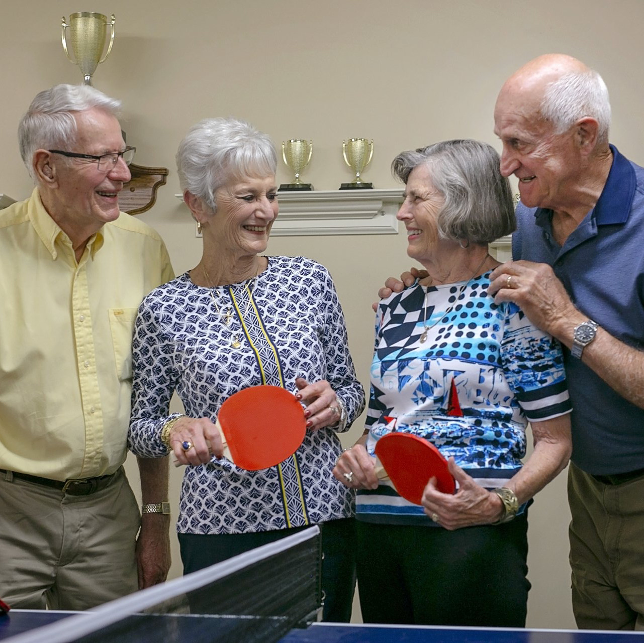 Active, senior living residents talking after playing a game of ping pong at 55+ community